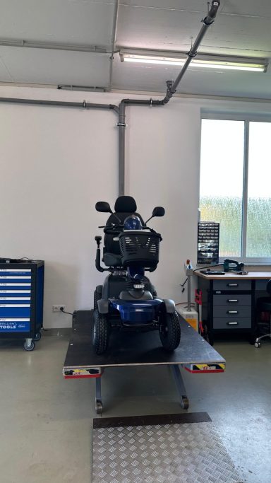 Ein blauer Motorroller auf einem Tisch in einer Werkstatt mit Werkzeugen im Hintergrund.